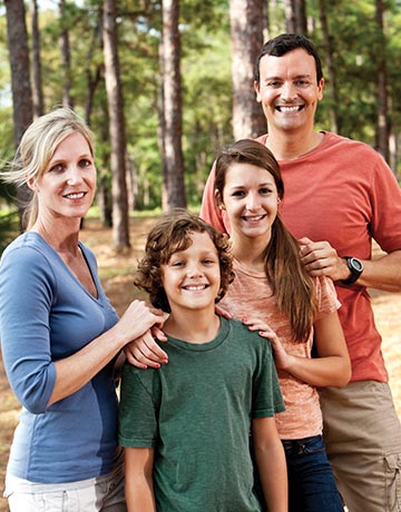 Family of four smiling with dense forest in background