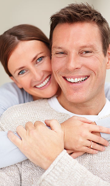 Couple in sweaters smiling at camera and embracing