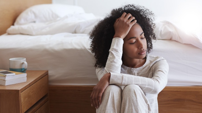 young african american woman sitting next to bed tired from sleep apnea