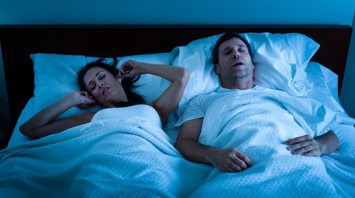 couple in bed man snoring because of sleep apnea woman covering her ears