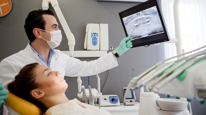 brunette woman in dental chair looking at dental X-ray with dentist pointing to image