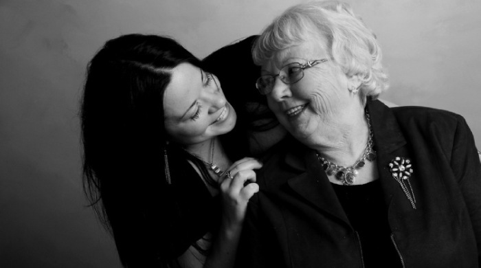 dark haired granddaughter leaning over embracing and smiling at her grandmother