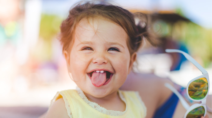 baby girl sticking out her tongue showing two baby teeth