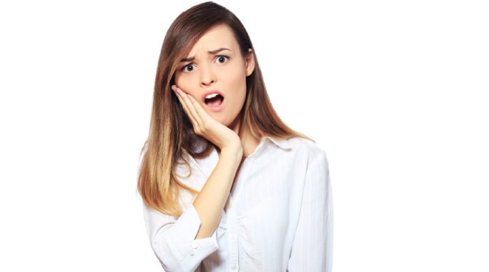 brown haired girl wearing a white shirt holds her mouth in pain because she needs a dental crown