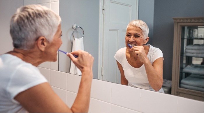 elderly woman brushing her teeth in front of a mirror