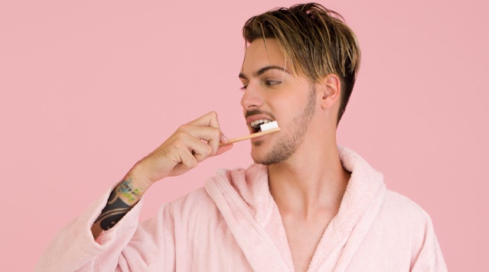 man wearing a bathrobe brushes his teeth to combat yellow teeth