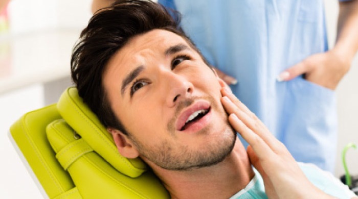 man in the dentist's chair holding his jaw before root canal therapy