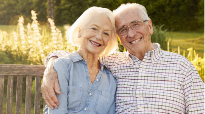 senior couple sitting on a bench hugging and smiling after learning their dental bridges can be repaired