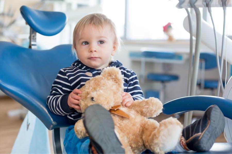 young child sitting in the dentist chair holding a stuffed bear