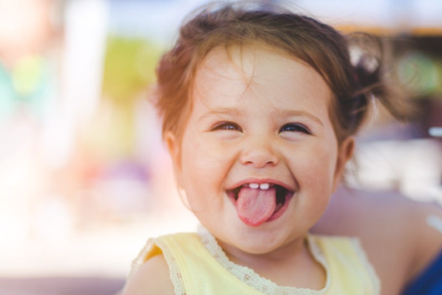 baby girl smiles and sticks out her tongue showing off two front baby teeth