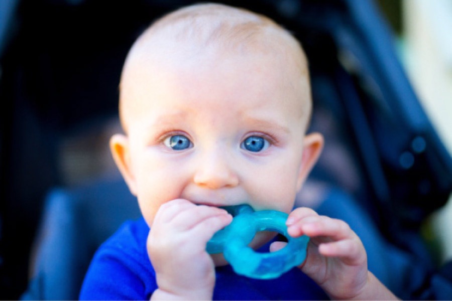 baby boy with blue eyes chewing on a blue plastic toy