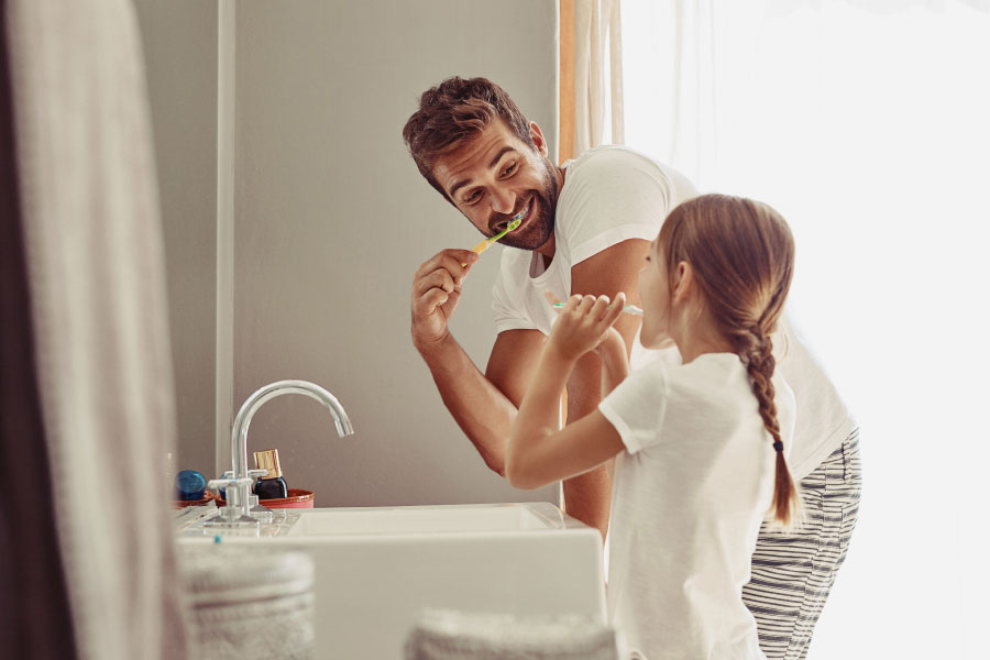 man brushing his teeth with his young daughter