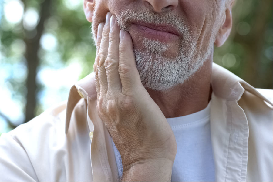 man with grey stubble holds his jaw in pain from TMJ/TMD