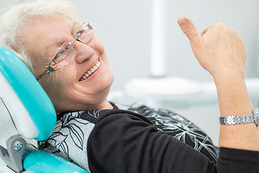 senior woman in the dentist's chair gives a thumbs up after getting a fixed dental bridge