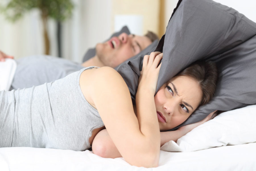 woman covers her head with a pillow to block out her partner's sleep apnea induced snoring.