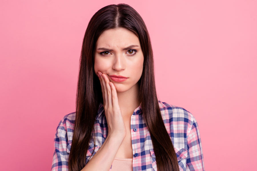 young dark haired woman holds her jaw with sensitive teeth